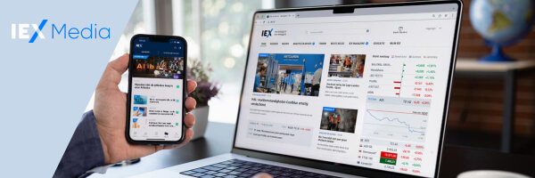 IEX Media. Mannelijke hand die een smartphone toont met de IEX App, op de achtergrond een laptop met de IEX.nl homepage op een donker bureau.