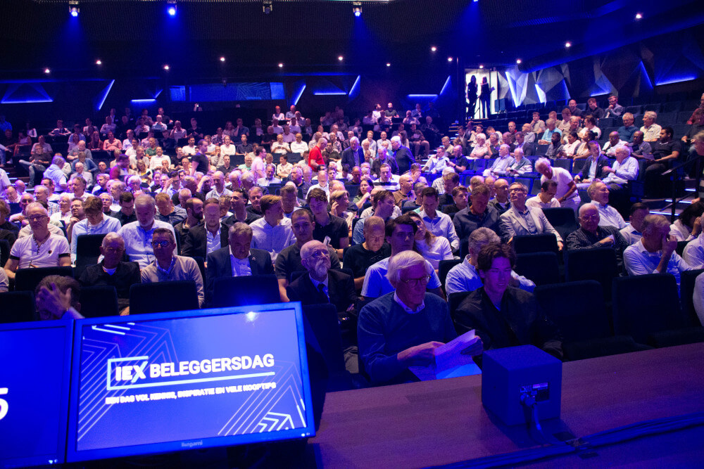 een zaal met publiek, in blauwe verlichting, gezien vanaf podium