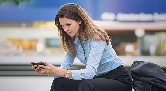 jonge vrouw in zakelijke kleding die buiten zit en naar een tablet kijkt
